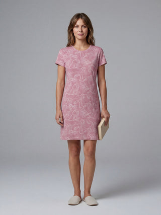 A woman in a pink floral print t-shirt dress and slippers holds a book.