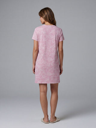 A woman stands facing away from the camera in a pink t-shirt style nightgown with a white floral print.