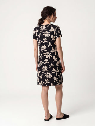 A woman in a black floral print sleep dress and black slippers, facing away from the camera.