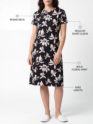 A woman stands posing in a black and white floral print knee-length dress.