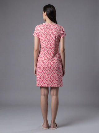 Woman standing, wearing a pink floral print t-shirt dress and cream slippers.