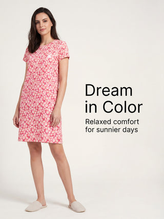 A woman in a pink floral print short sleeve nightgown and slippers stands posing.