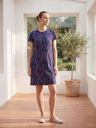 A woman stands facing forward wearing a navy blue short-sleeved nightgown with a pink and grey wavy stripe print and beige slippers.