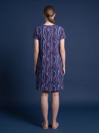 A woman stands with her feet apart, wearing a dark blue sleep dress with an abstract print of pink and light blue vertical stripes, a round neck, and short sleeves.