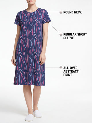 A woman stands with her feet apart, wearing a dark blue sleep dress with an abstract print of pink and light blue vertical stripes, a round neck, and short sleeves.
