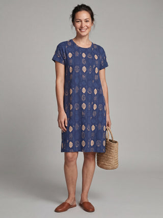 Woman wearing a blue short-sleeve A-line dress with a geometric print and holding a straw bag.