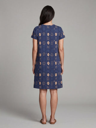 Women in a blue, short-sleeved, knee-length dress with a geometric pattern, viewed from the back, standing.