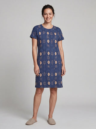 Women in a blue, short-sleeved, knee-length dress with a geometric pattern, standing and smiling.