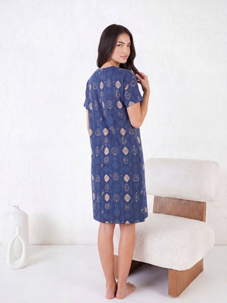 A woman stands turned away from the camera, showing off her blue, geometric-print sleep dress.