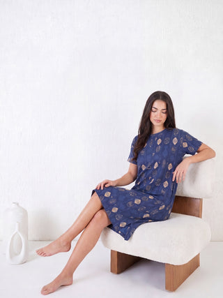 A woman sits on a chair wearing a blue sleep dress with a geometric print.