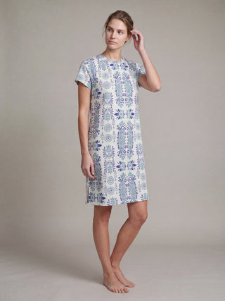 A woman stands wearing a blue and white printed sleep dress with short sleeves.