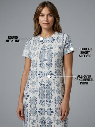 A woman stands wearing a blue and white printed sleep dress with short sleeves.