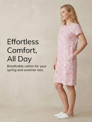 A woman poses in a light pink sleep dress with a white geometric print and white slippers, with text that reads "Effortless Comfort, All Day. Breathable cotton for your spring and summer rest."