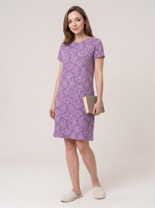 Women in a purple patterned sleep dress and slippers, holding a book.