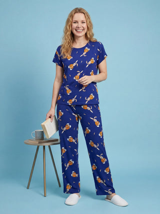 Woman in blue pajamas with a bunny print, posing while holding a book next to a small table.