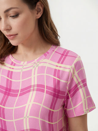A woman poses for a product shot wearing a pink plaid t-shirt, perfect for a comfortable sleepwear collection.