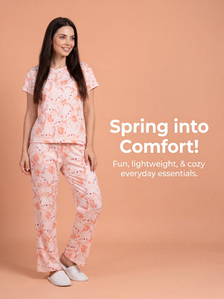 A woman poses in a pink flamingo-print pajama set with white slippers, with text that reads "Spring into Comfort! Fun, lightweight, & cozy everyday essentials."