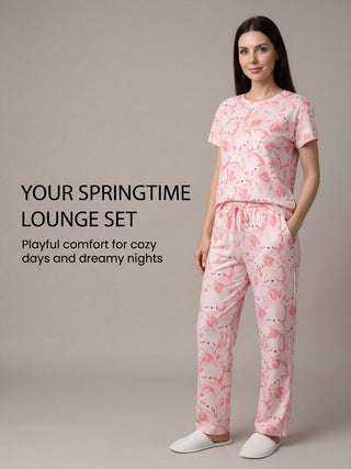 Woman in a pink pajama set with a flamingo print, standing with her hands in her pockets.