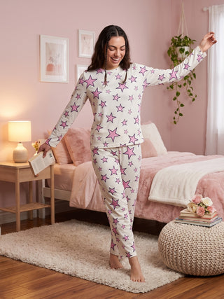 A woman in white pajamas with pink stars is laughing with her hand on her hip.
