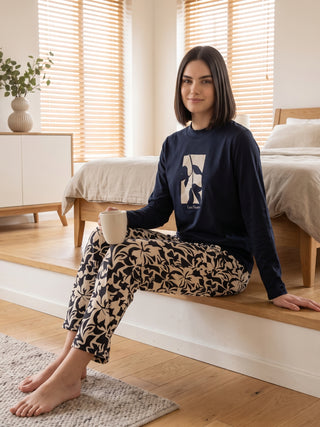 A woman sits on a wooden step wearing navy blue pajamas with a floral print.