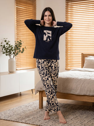 A woman in navy blue long-sleeved pajamas with a botanical print poses with her hands behind her head.
