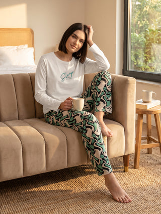 Woman lounging on a sofa wearing a white long-sleeved top with "Sleep solves everything" text and green and black printed pants.