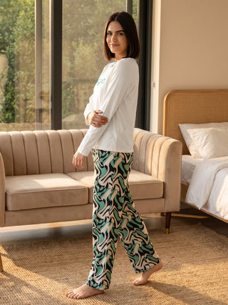 Women in a relaxed pose, wearing a white long-sleeved top with blue text and patterned pajama pants with a swirl print in green, black, and beige.