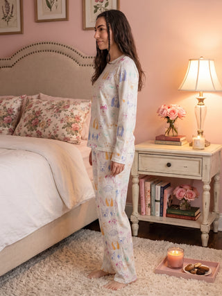 A woman poses standing in a white pajama set with a colorful dog print.
