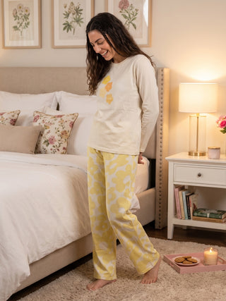 Woman in yellow floral pajamas standing on a fluffy rug next to a bed.