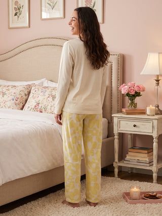 A woman in a cream long-sleeved pajama top with yellow floral pants stands facing away from the camera.