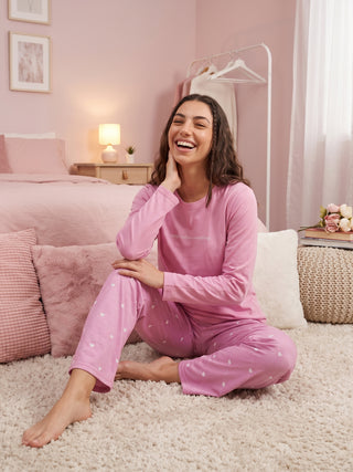 A young woman in pink heart-print pajamas laughs while sitting on a fluffy rug.