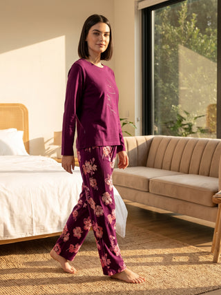 A woman in a plum-colored, floral-print pajama set walks across a bedroom floor.