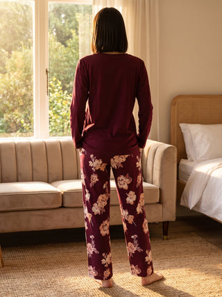 Women's long-sleeve burgundy floral print pajama set, standing with back to camera.