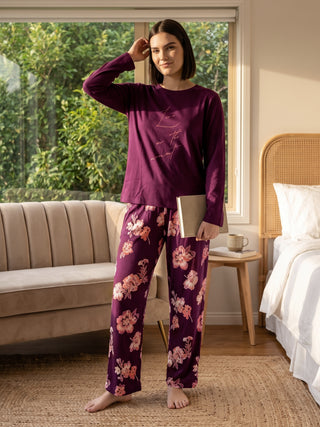 A woman in a plum pajama set with a floral print, standing with her hand on her head.