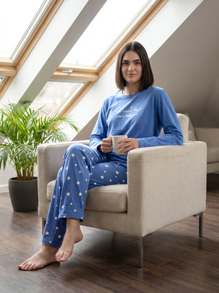A woman in blue star-print pajamas sits comfortably in a chair, holding a mug.