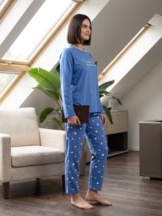 Women in a blue long-sleeved pajama set with white stars, standing with a book in hand.