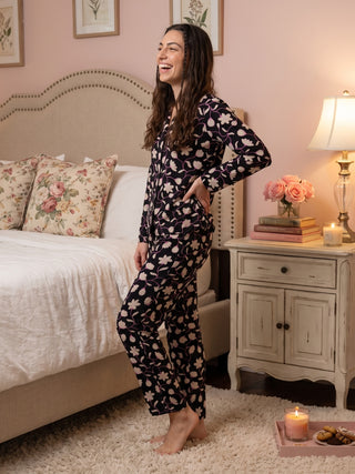 A woman models a black pajama set with a floral print, standing with her hand on her hip.
