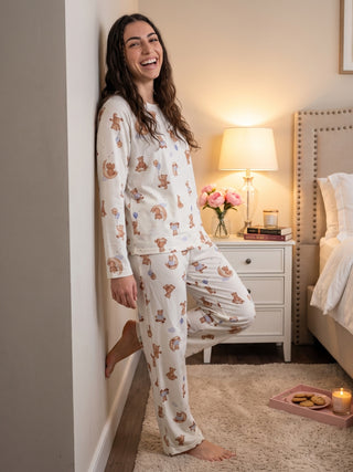 A woman stands wearing cream-colored pajamas with a teddy bear print, leaning against a wall.