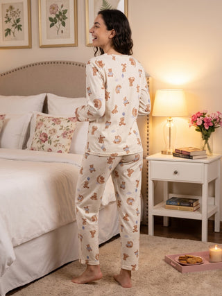 A woman in cream-colored pajama set with a teddy bear print stands facing away from the camera.