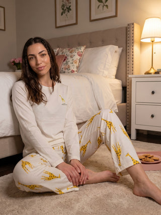 A woman sits on the floor in cream long-sleeved pajamas with a giraffe print.
