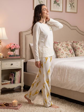 Woman in white long-sleeve pajamas with a giraffe print walks by a bed.