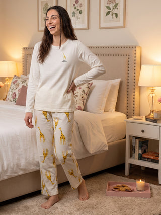 A woman stands in a bedroom wearing white long-sleeved pajamas with a giraffe print.