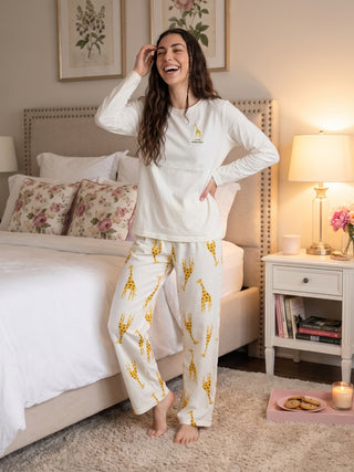 A woman stands laughing, wearing a cream pajama set with a giraffe print and a small giraffe graphic on the top.