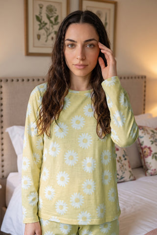 A young woman poses in her bed wearing a yellow daisy print pajama set.