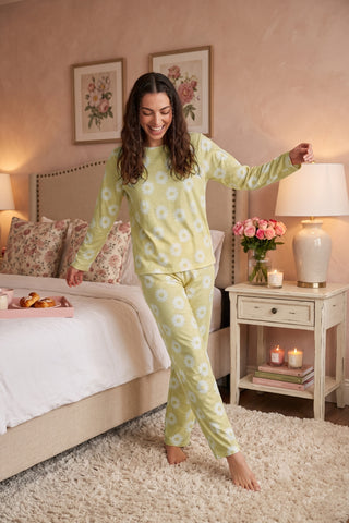 Woman in light yellow daisy print pajamas, standing on a cream shag rug next to a bed.
