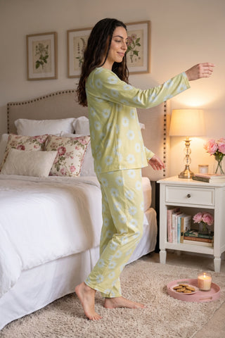A woman in a yellow daisy-print pajama set stands with her arm outstretched.