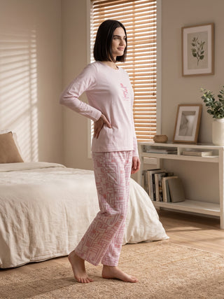 Women's light pink long-sleeved pajama set with a geometric pattern, posing with hand on hip.