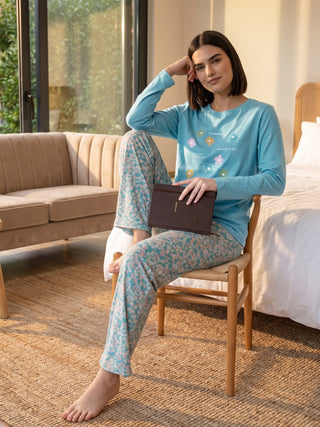 A woman sits on a chair wearing light blue floral print pajamas.