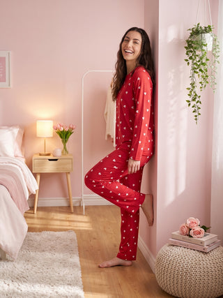 Woman in red heart-print pajamas leaning against a pink wall.