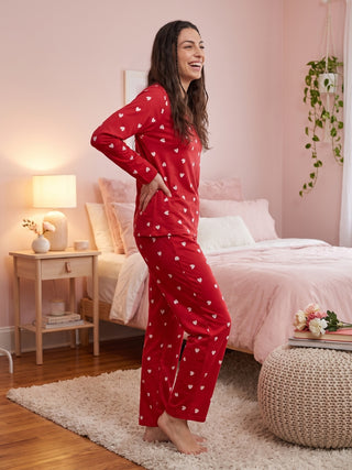 A woman with a happy expression poses wearing red heart-printed pajamas.